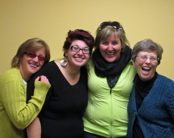 Denise Guitar, Dominique Manuel, Josee Martin and Dona Sauerburger stand in front of a wall with arms around each other, laughing.
